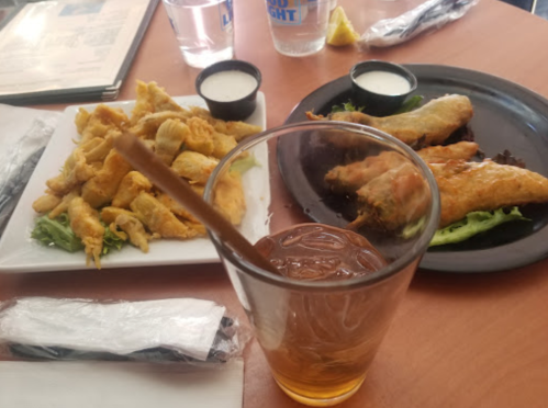 A table with a glass of iced tea, a plate of fried food, and another plate with spring rolls and dipping sauce.